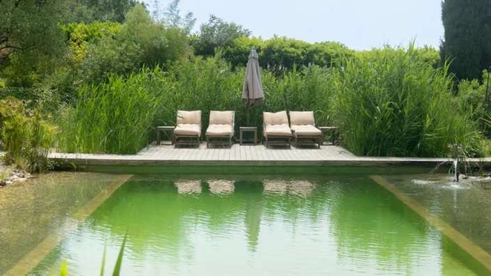 Liegestühle stehen auf einem Holzdeck neben einem grünen Pool