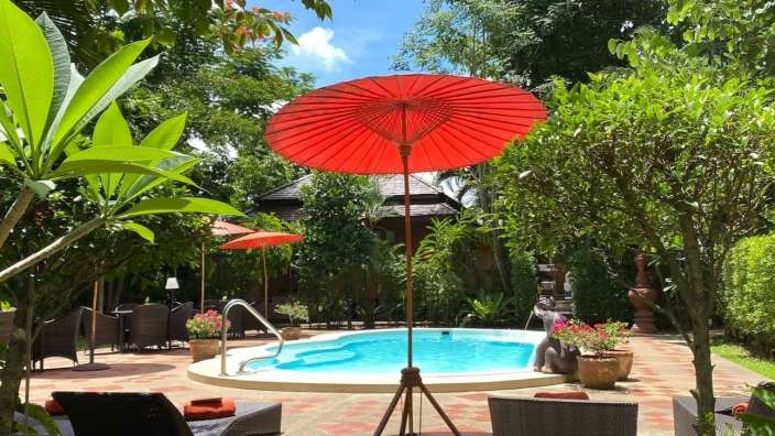 Ein großer roter Regenschirm steht vor einem Swimmingpool
