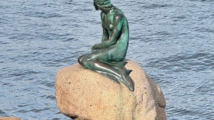 Eine Statue einer Meerjungfrau sitzt auf einem Felsen im Wasser