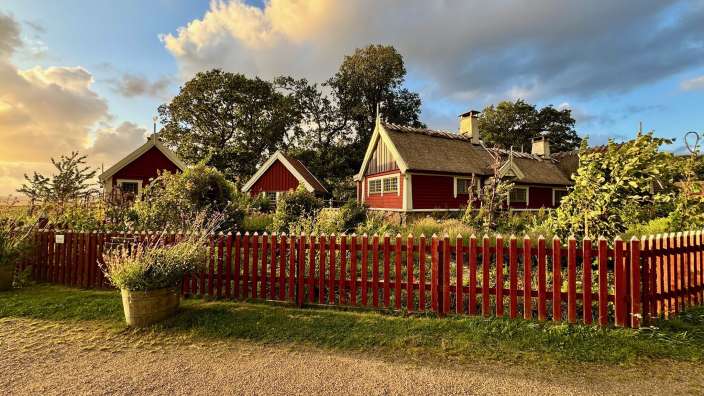 Ein kleines rotes Haus mit Strohdach steht hinter einem roten Zaun