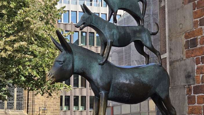 Eine Statue eines Esels, eines Huhns, eines Schafes und eines Hundes steht vor einem Backsteingebäude