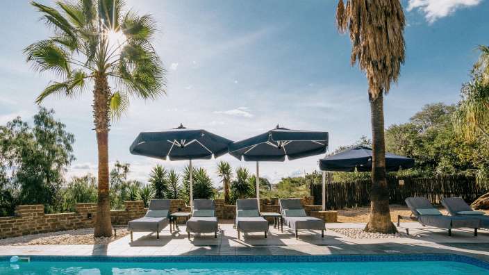 Liegestühle und Sonnenschirme um einen Swimmingpool an einem sonnigen Tag