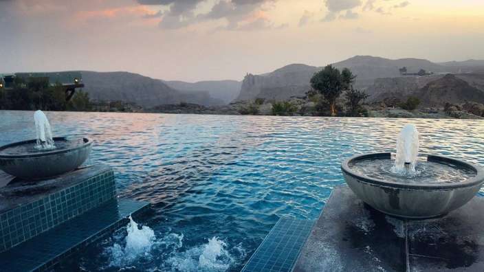 Ein Infinity-Pool mit zwei Brunnen und einem Berg im Hintergrund