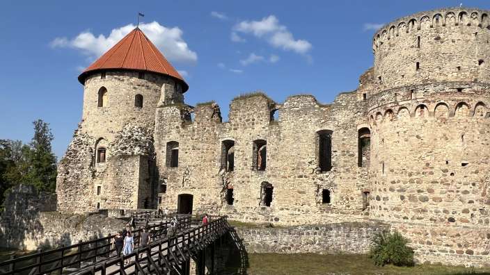 Eine Gruppe von Menschen steht auf einer Holzbrücke in der Nähe eines großen Steingebäudes