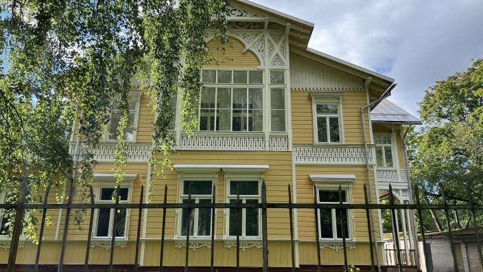 Ein gelb-weißes Haus mit vielen Fenstern und einem Zaun davor