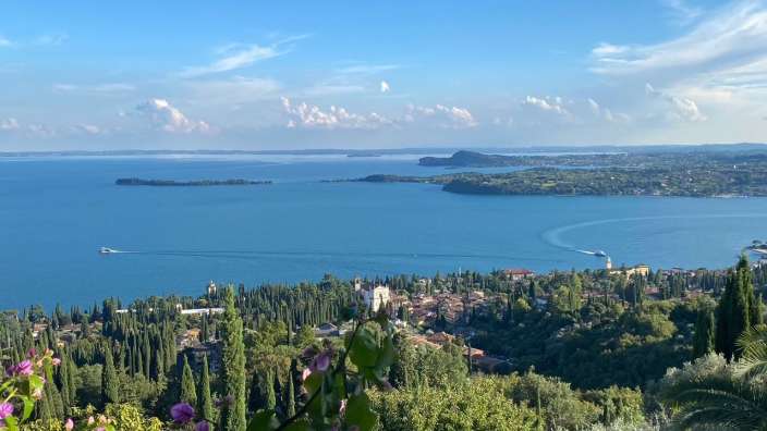 Blick aus dem Hotelfenster auf den Gardasee Ein Blick auf einen See mit einer kleinen Insel im Hintergrund