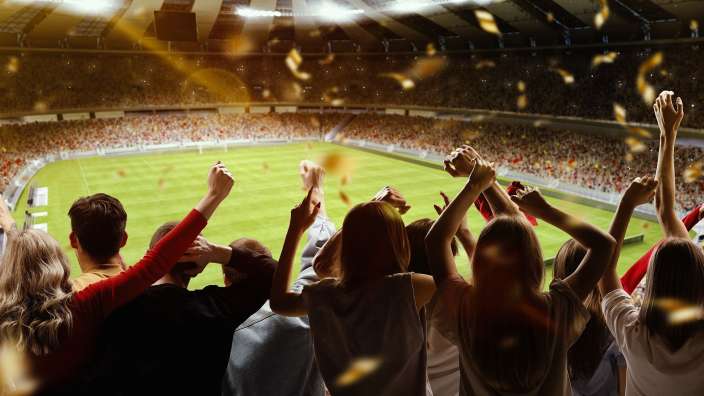 Eine Gruppe von Menschen hält ihre Hände in die Luft, während sie ein Fußballspiel sehen