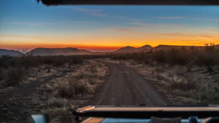 Gamedrive I Madikwe Eine unbefestigte Straße mit Bergen im Hintergrund bei Sonnenuntergang