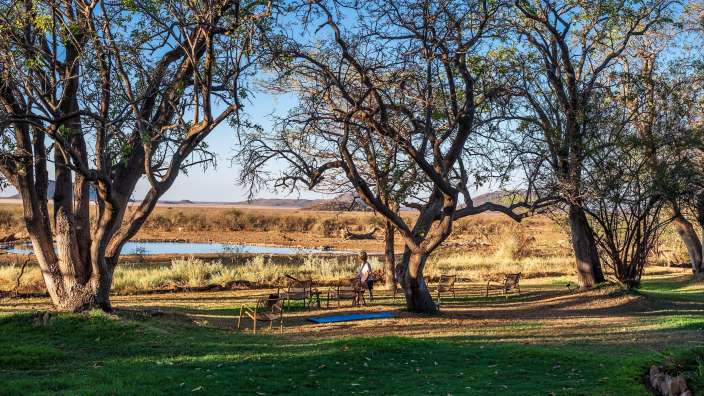 Last Word Madikwe I Garten Eine Frau steht auf einer Yogamatte in einem Feld neben einem Fluss
