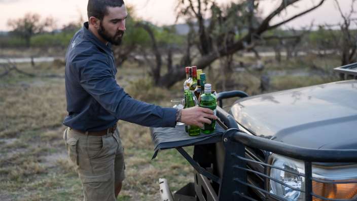 Gamedrive I Drink zum Sonnenuntergang Ein Mann hält eine Flasche Whisky neben einem Auto