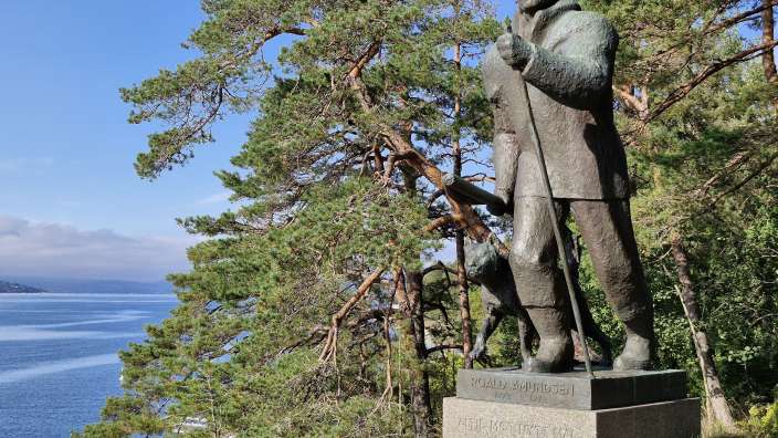Eine Statue eines Mannes und eines Hundes steht vor einem See