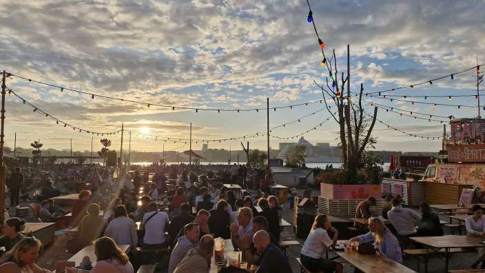 Eine Gruppe von Menschen sitzt an Bänken und Tischen in einem Park