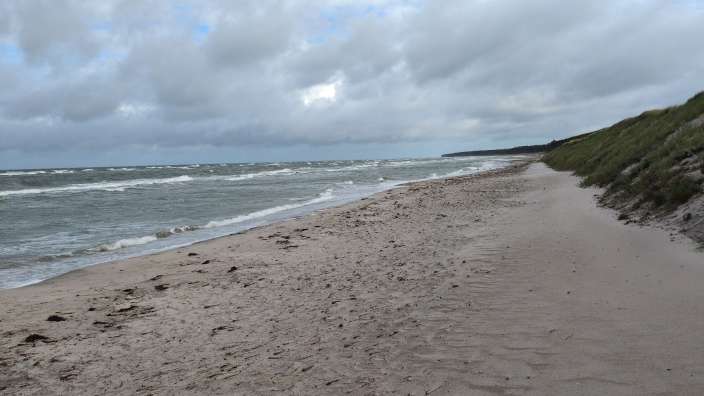 Ein Strand mit Sand und seichtem Wasser unter einem bewölkten Himmel.
