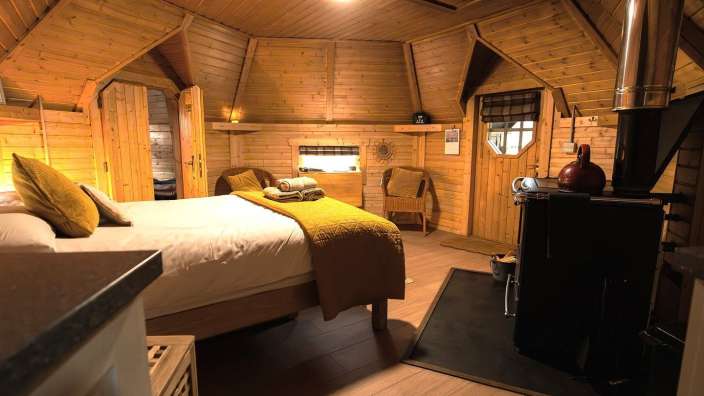 Das Bild zeigt ein gemütliches Schlafzimmer mit Holzwänden und einer Eckbank vor einem Ofen.