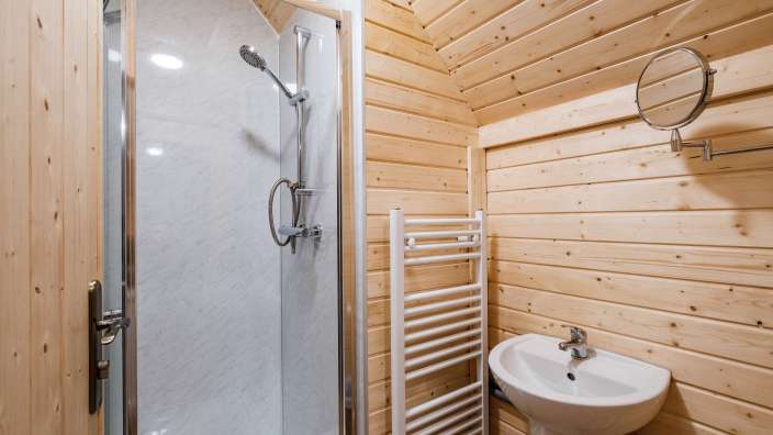 Ein Badezimmer mit Holzwänden und einer Duschkabine ist mit einem Waschbecken, einem Handtuchwärmer und einem Spiegel ausgestattet.