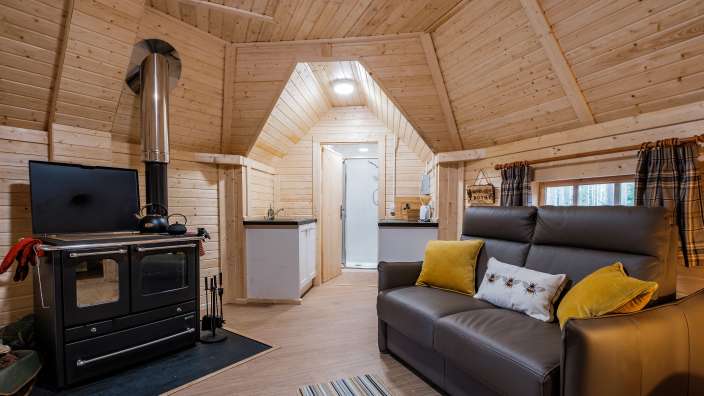 Ein gemütliches Holzhaus mit Wohnbereich, Küche und einer Dusche, beleuchtet durch eine Deckenlampe.