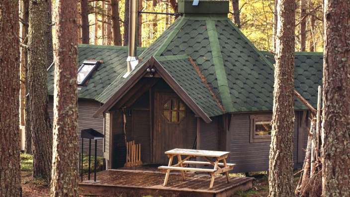 Ein kleines Holzhaus mit einem grünen Schindeldach steht inmitten eines Waldes.