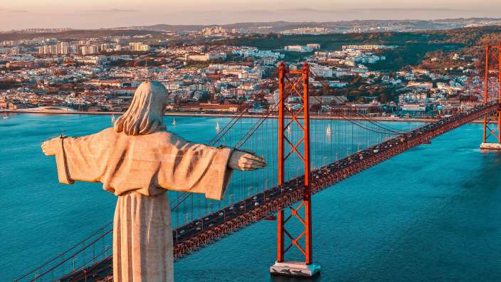 Die Statue Christi des Königs steht über der Stadt Lissabon mit der Ponte 25 de Abril im Hintergrund bei Sonnenaufgang.