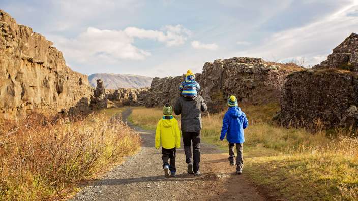 Ein Vater mit seinen beiden Kindern geht auf einem Schotterweg durch eine felsige Landschaft.