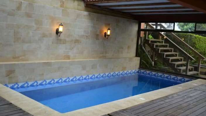 Ein kleiner Pool unter einem Holzdach mit Glaselementen, daneben Außentreppen.