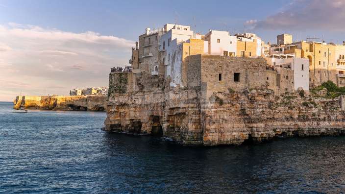 Ein Dorf mit weißen Häusern ist auf einer Klippe am Meer gebaut, das im Abendlicht beleuchtet wird.