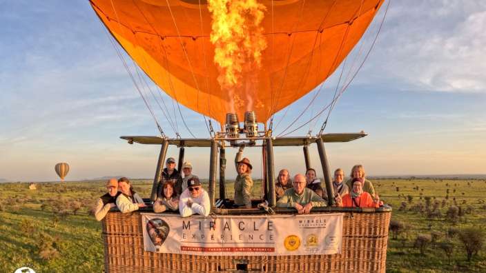 Eine Gruppe von Menschen genießt eine Fahrt mit einem Heißluftballon über der afrikanischen Savanne bei Sonnenuntergang.