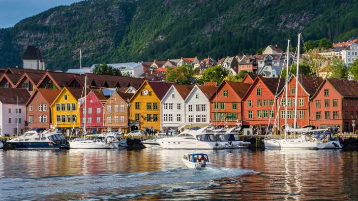 Die bunten Hansehäuser von Bryggen in Bergen spiegeln sich im Wasser, während Yachten und ein Motorboot im Hafen liegen.