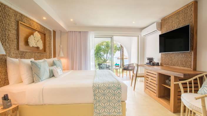 Ein gut beleuchtetes Hotelzimmer mit einem großen Bett, einem Fernseher und einem Blick auf das Meer.