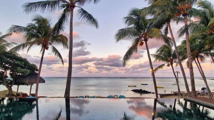 Ein Infinity-Pool spiegelt den Himmel und Palmen in dieser tropischen Strandlandschaft.