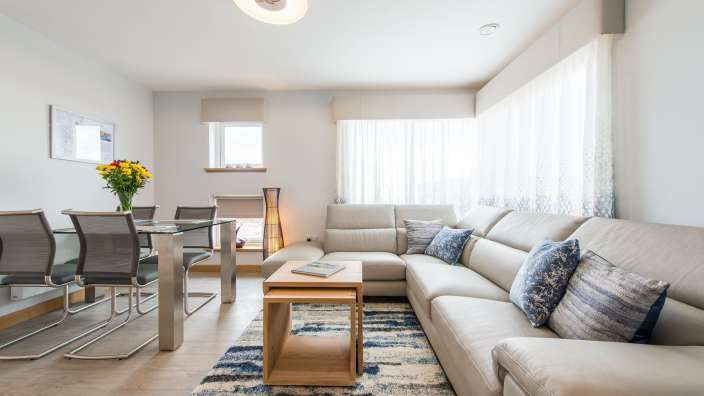 Ein helles Wohnzimmer mit einem Esstisch, einer Couch und einem Teppich.
