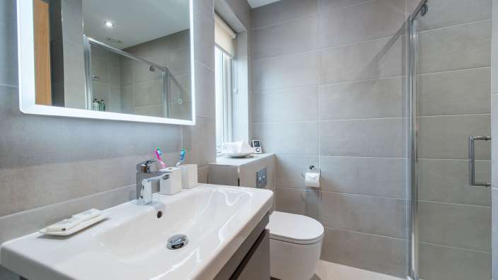 Eine moderne, geflieste Toilette, ein Waschbecken und eine Duschkabine sind in diesem gut beleuchteten Badezimmer zu sehen.