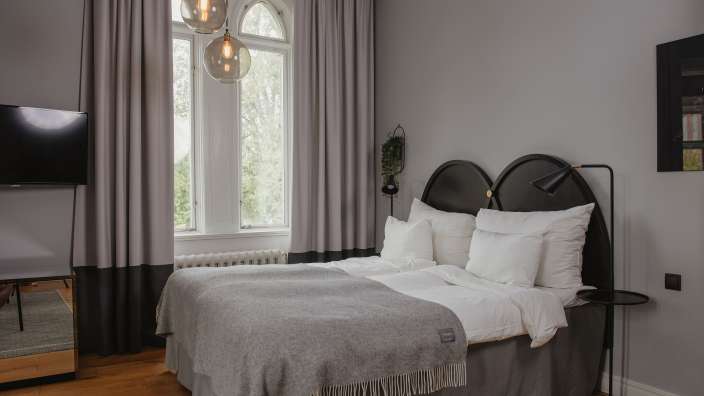 Ein Schlafzimmer mit einem Bett, Fernseher, Vorhängen, einem Fenster und einem Gemälde.