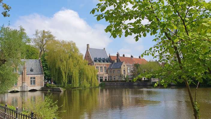 Ein idyllischer Kanal mit historischen Gebäuden und üppigem Grün unter blauem Himmel mit weißen Wolken.