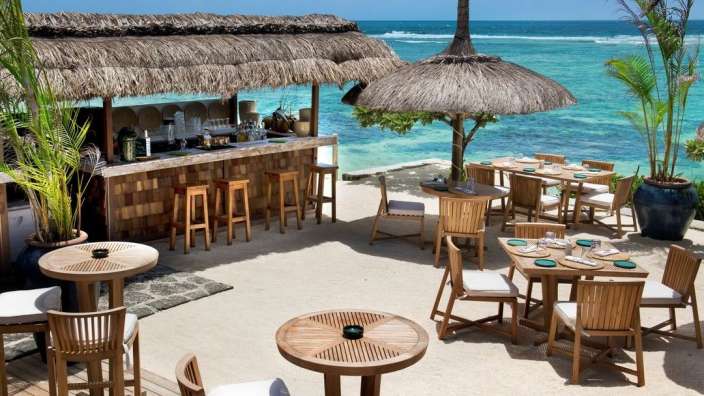 Auf diesem Bild ist ein Restaurant am Strand mit Tischen, Stühlen und einer Bar am Meer zu sehen.