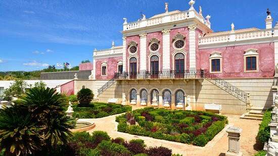 Ein prunkvolles rosa Barockschloss mit kunstvoll gestalteten Gärten und einem blauen Himmel.