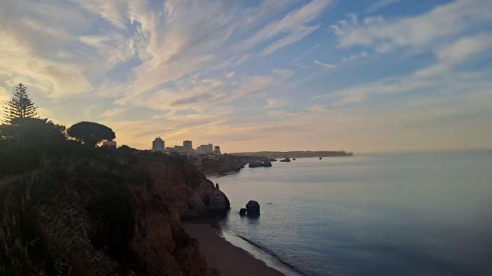Ein Sonnenuntergang über einer Küstenstadt mit Felsen und dem Meer.