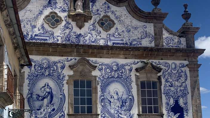 Eine detailreiche Fassade eines Gebäudes ist mit blauen und weißen Fliesen bedeckt, die im Barockstil kunstvolle Muster und religiöse Szenen darstellen.