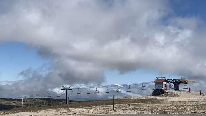 Eine Skiliftanlage mit mehreren Sitzen transportiert auf einer Berglandschaft mit bewölktem Himmel.