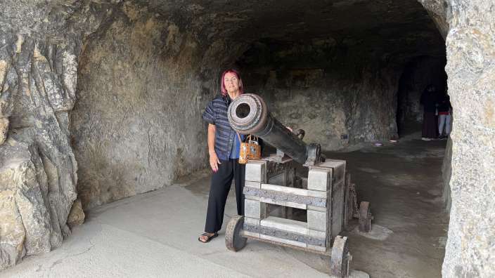 Eine Frau mit roten Haaren steht in einer Felsenhöhle neben einer alten Kanone.