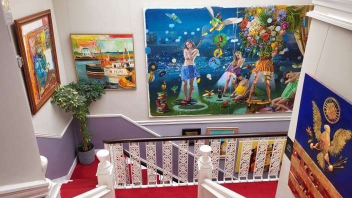 Die obere Etage einer Treppe mit rotem Teppich und einer Ansammlung von Kunstwerken an den Wänden.