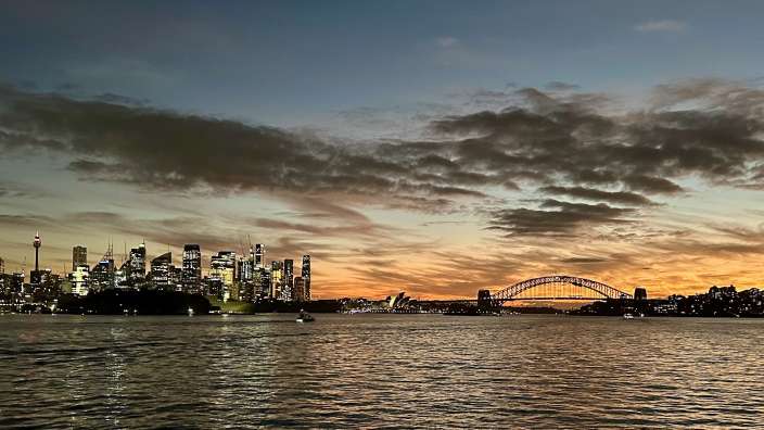 Eine beleuchtete Skyline von Sydney im Abenddämmerungshimmel mit dem Sydney Harbour Bridge.
