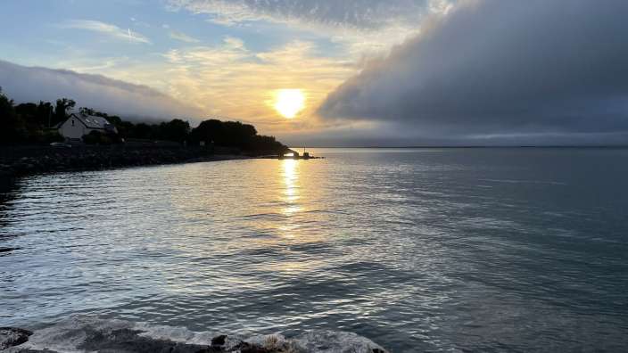 Ein Sonnenuntergang über dem Wasser mit einer bewohnten Küste und einer großen Wolkenformation.
