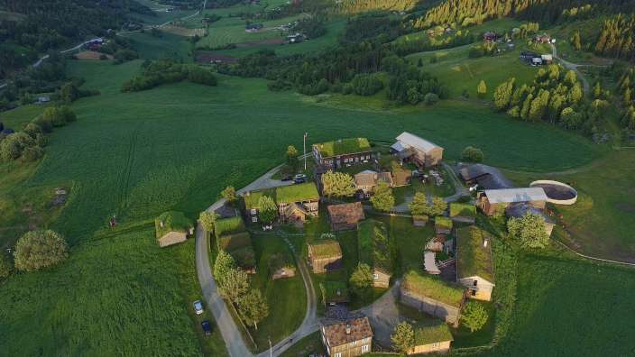 Ein malerisches Dorf mit traditionellen Gebäuden, die mit grünen Grasdächern gedeckt sind, liegt eingebettet in einer weitläufigen grünen Landschaft.