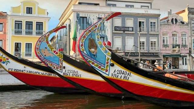Fünf traditionell bemalte Boote liegen in einem Kanal vor bunten Gebäuden.
