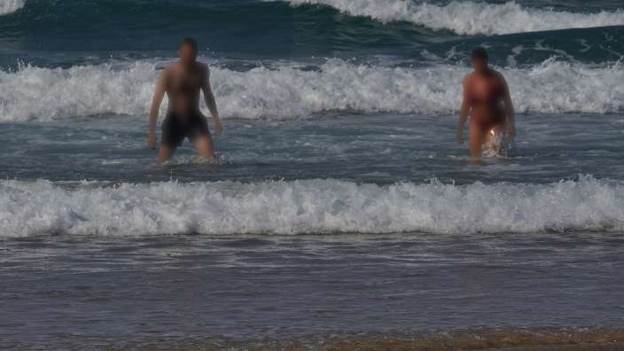 Zwei Personen stehen im Meer und es brechen Wellen.