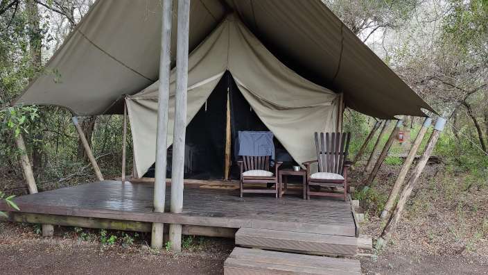 Übernachtungszelt im Rhino Plains Camp auf einer hölzernen Plattform mitten in einer bewaldeten Naturlandschaft.