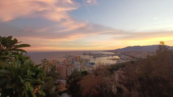 Blick vom Balkon des Parador de Málaga Gibralfaro in der Abenddämmerung über die Stadt und den Hafen.