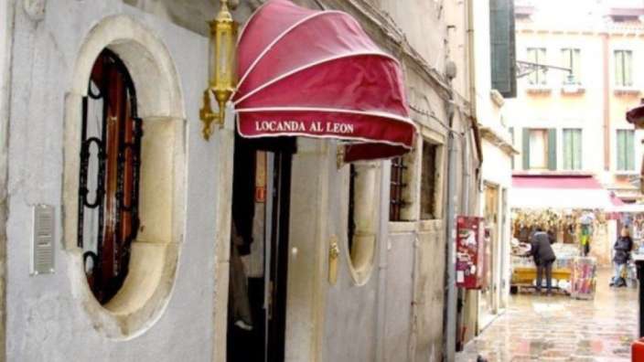 Ein rot-weißer Regenschirm hängt an einem Gebäude und sagt locanda al leon