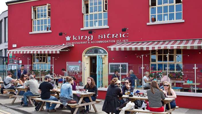 Eine Gruppe von Menschen sitzt an Picknicktischen vor einem Restaurant namens king sitric