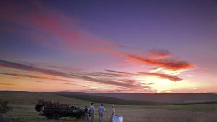 Eine Gruppe von Menschen steht vor einem LKW in einem Feld bei Sonnenuntergang